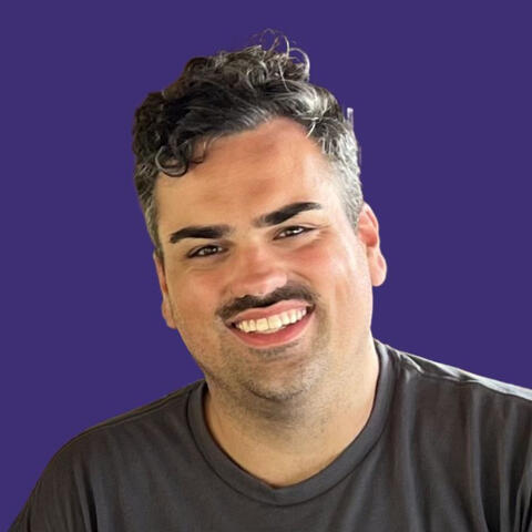headshot of John Kliewer smiling against a blue background wearing a dark grey t-shirt